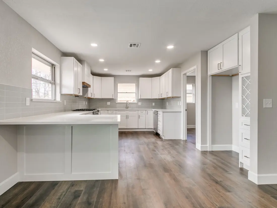 The same kitchen finished: new white cabinets, stone counters, tiled backsplash and new wood floors.