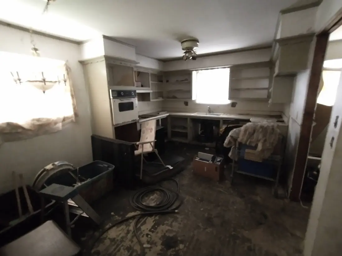 A kitchen left vacant for years: cabinets torn out, bare counters, and belongings still scattered across the floor.